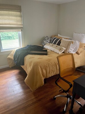 Un dormitorio con cama, una silla, un escritorio y una ventana con persianas.