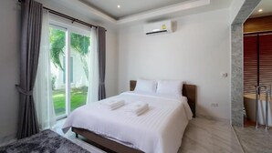 A modern hotel room with a bed, a window with curtains, an air conditioning unit, and a view of greenery outside. - Orchid Paradise Homes OPV429 (Hin Lek Fai)
