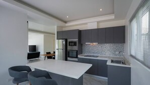 A modern kitchen with grey cabinets, a white countertop, and a built-in island with bar stools. - Orchid Paradise Homes OPV429 (Hin Lek Fai)