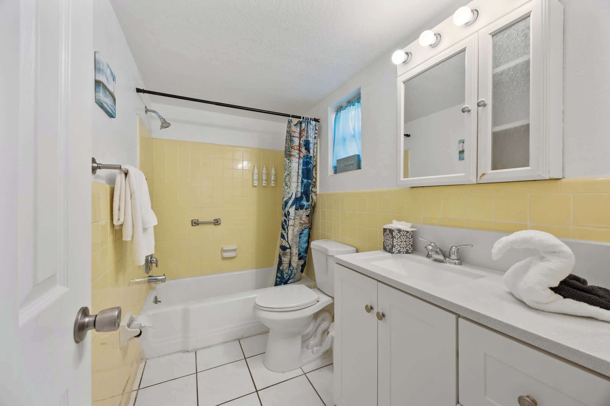 Une salle de bain avec une baignoire, des toilettes et un lavabo, des carreaux jaunes et un miroir au-dessus du lavabo.