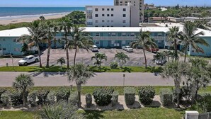 A hotel with a parking lot, palm trees, and a view of the beach. - Cozy 1BR Ground Floor Apartment Steps to Beach (Cocoa Beach)