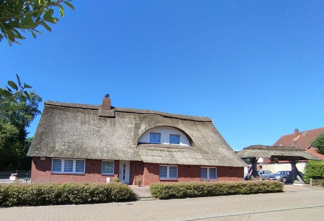 Ein Haus mit einem Reetdach und einem Backsteinfundament, einem kleinen Veranda und blauem Himmel.