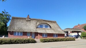A thatched-roof house with a brick base, a small porch, and a clear blue sky. - Vacation apartment ELBE in Relax - Belum near Otterndorf LK Cuxhaven with pool use (Belum)