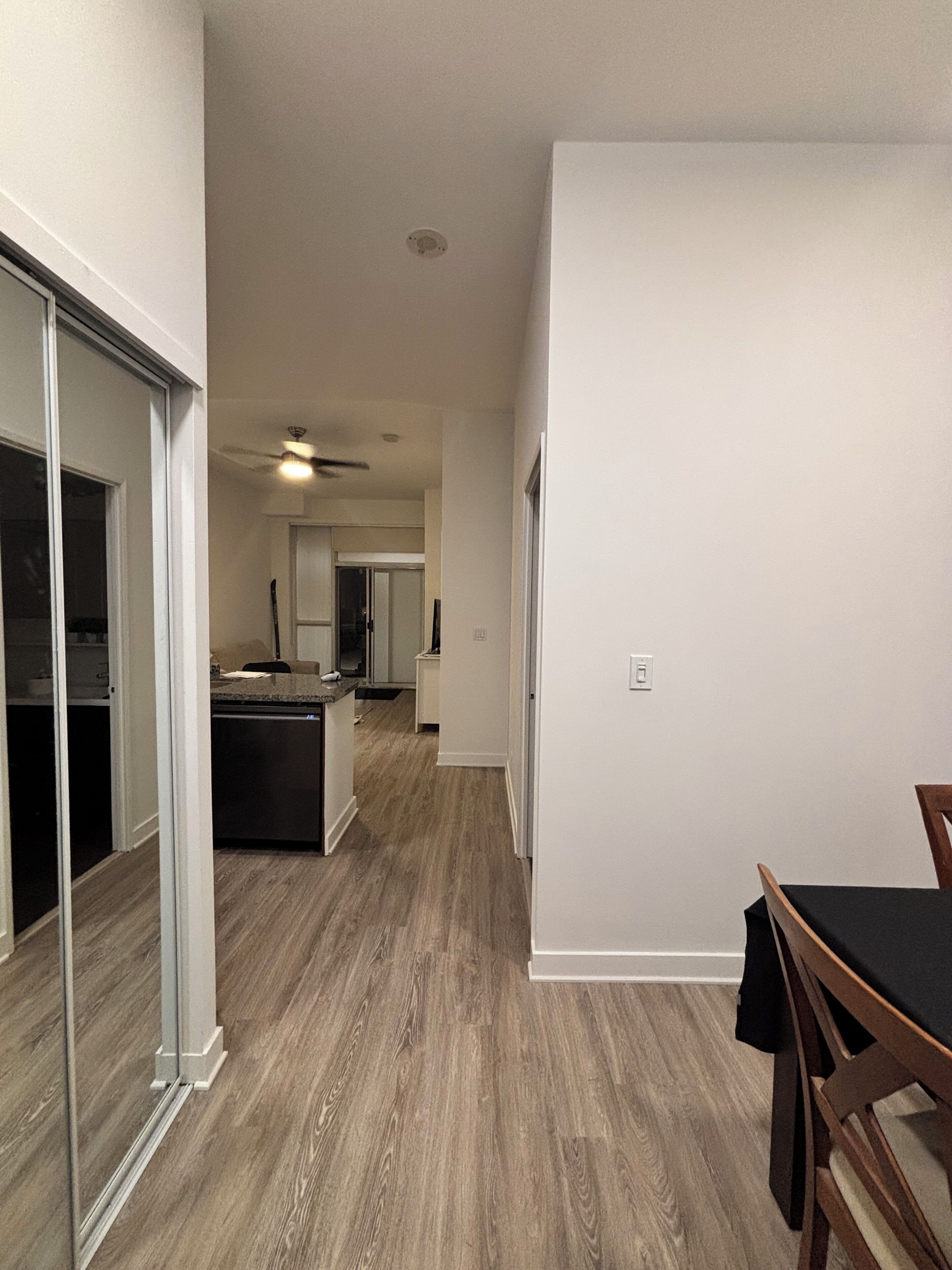 A modern kitchen with a central island, a dining area with a table and chairs, and a hallway leading to a bedroom.