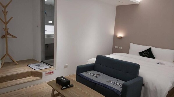 Une chambre d’hôtel avec un lit, un canapé, une petite table avec une télécommande et un porte-manteau.