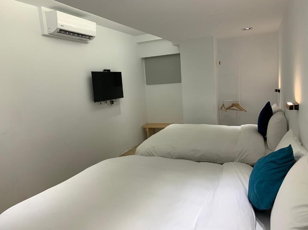 A hotel room with a bed, a TV, an air conditioner, a coat rack, and a door.