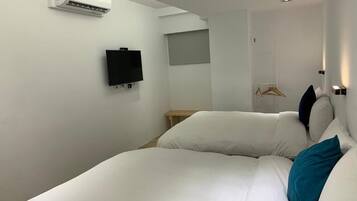 A hotel room with a bed, a TV, an air conditioner, a coat rack, and a door.