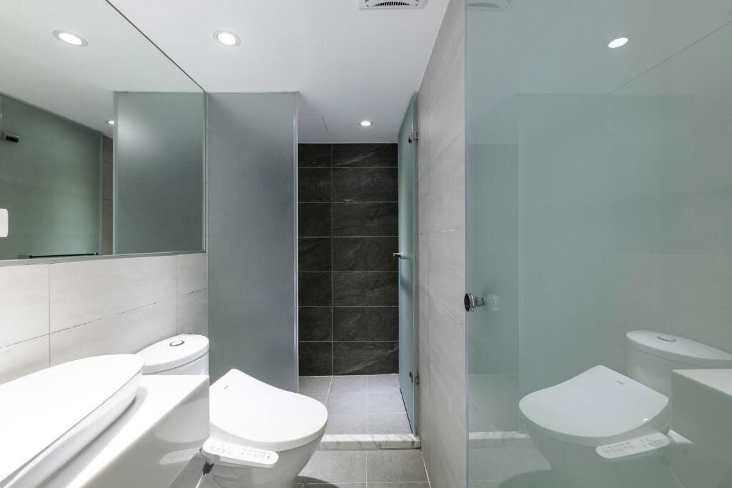 A modern bathroom with a glass shower enclosure, a separate toilet, and a vanity with a mirror.