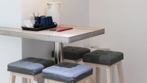 Zona pranzo con tavolo bianco, sgabelli imbottiti neri e lampada a sospensione.