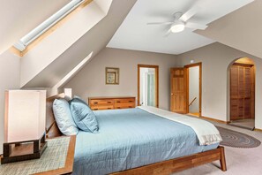 A bedroom with a sloped ceiling, a bed with a wooden headboard, a bedside table, and a ceiling fan. - Acadia National Park Haven-New! (Mount Desert)