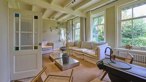 A spacious living room with a high ceiling, large windows, a sofa, a coffee table, and a fireplace. - Luxury farmhouse with sauna in Twente (Vriezenveen)