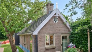 A small brick house with a gabled roof, a chimney, and a door with a window. - Luxury farmhouse with sauna in Twente (Vriezenveen)