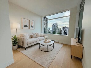 A modern living room with a sofa, coffee table, and a large window offering a city view. - Spectacular penthouse in a modernist, boutique concrete-and-glass building (Vancouver)
