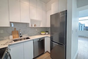A modern kitchen with white cabinets, a stainless steel refrigerator, a dishwasher, and a marble backsplash. - Spectacular penthouse in a modernist, boutique concrete-and-glass building (Vancouver)