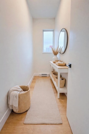 A hallway with a white bench, a mirror, baskets, and a rug. - Spectacular penthouse in a modernist, boutique concrete-and-glass building (Vancouver)