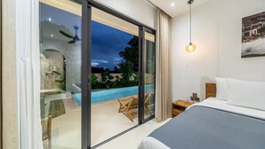 Un dormitori amb un llit gran, una tauleta de nit, una làmpada i vista a una piscina exterior.