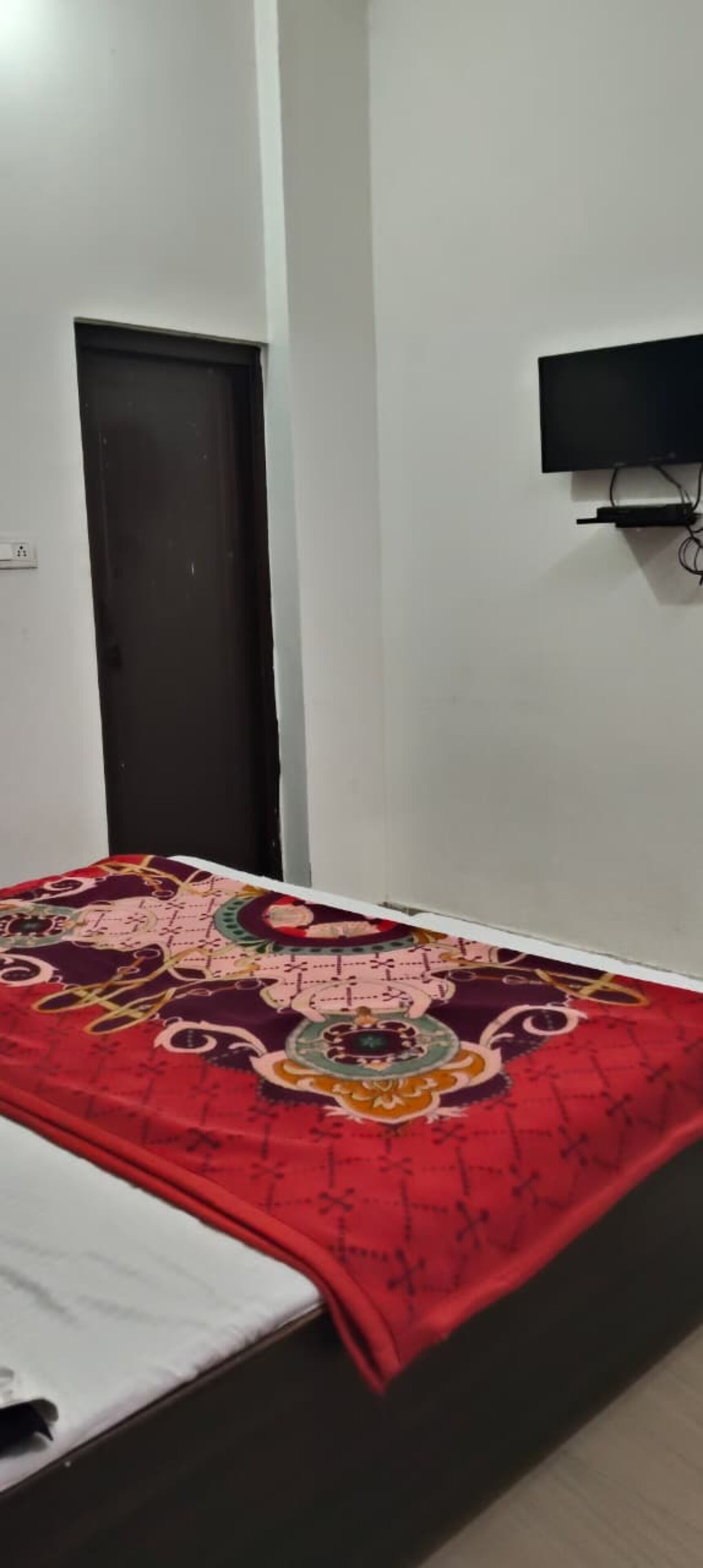 A bedroom with a bed, a television mounted on the wall, and a door.