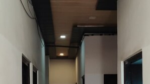 A corridor with a tiled floor, white walls, and black-painted doors. - Yuvraj Guest House (Rudrapur)
