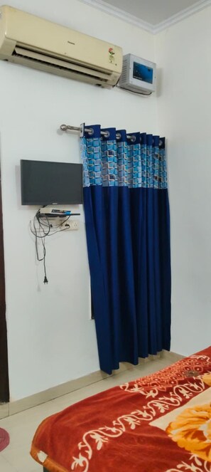Una habitación con cama, aire acondicionado, televisor y cortina.
