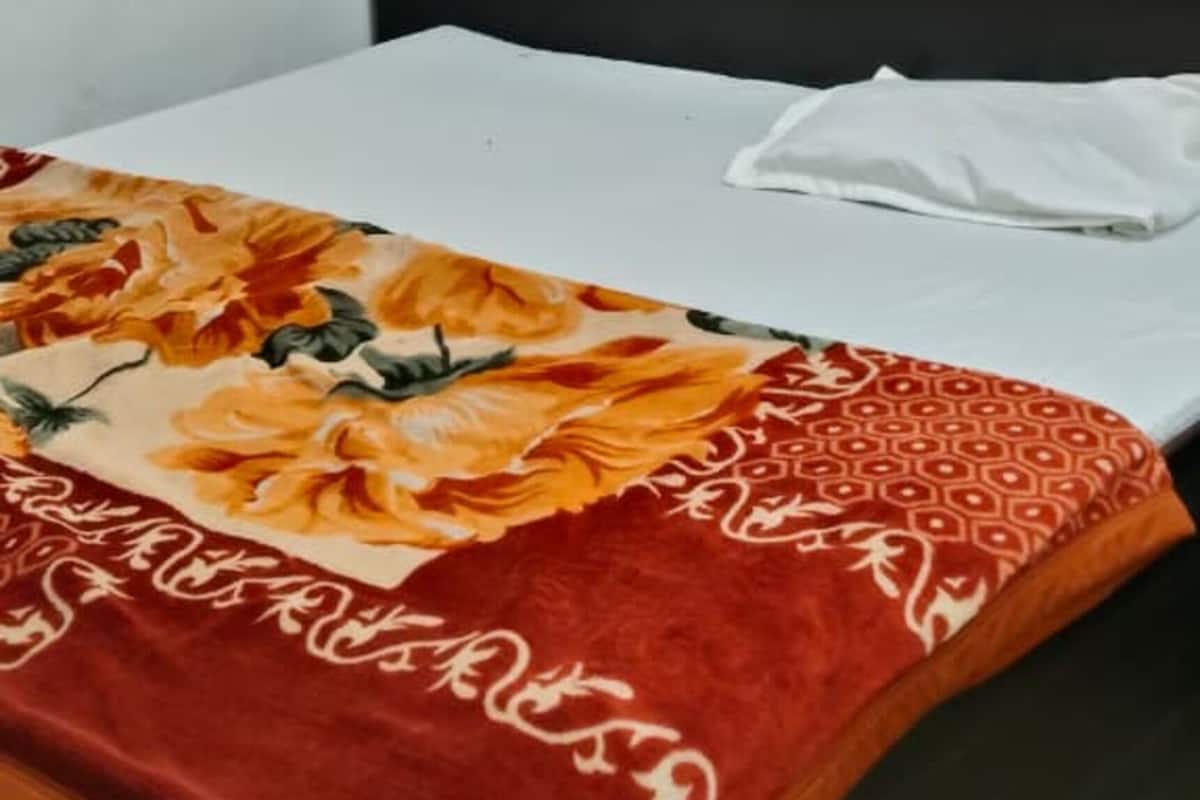 Una cama individual con una colcha de estampado floral, un cabecero negro y paredes blancas.