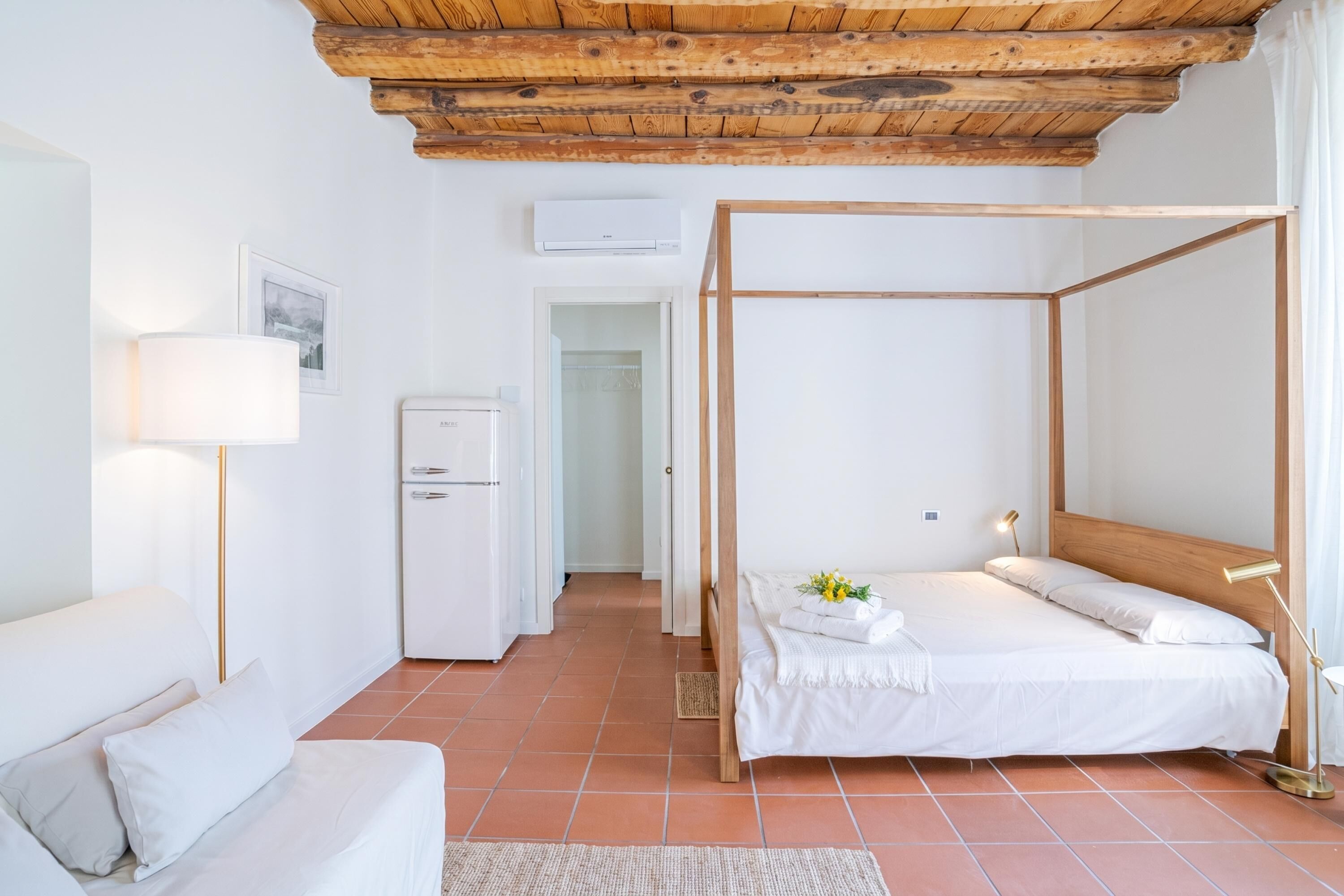 Une chambre à coucher avec un lit à baldaquin, un canapé blanc, une lampe de chevet et une petite table avec une lampe.