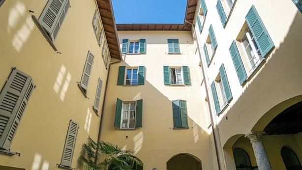 Un estrecho callejón flanqueado por edificios con arcos y numerosas ventanas con contraventanas.