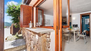 Um parapeito de pedra com uma porta de madeira, uma área de refeições com mesa e cadeiras, e vista para o exterior.