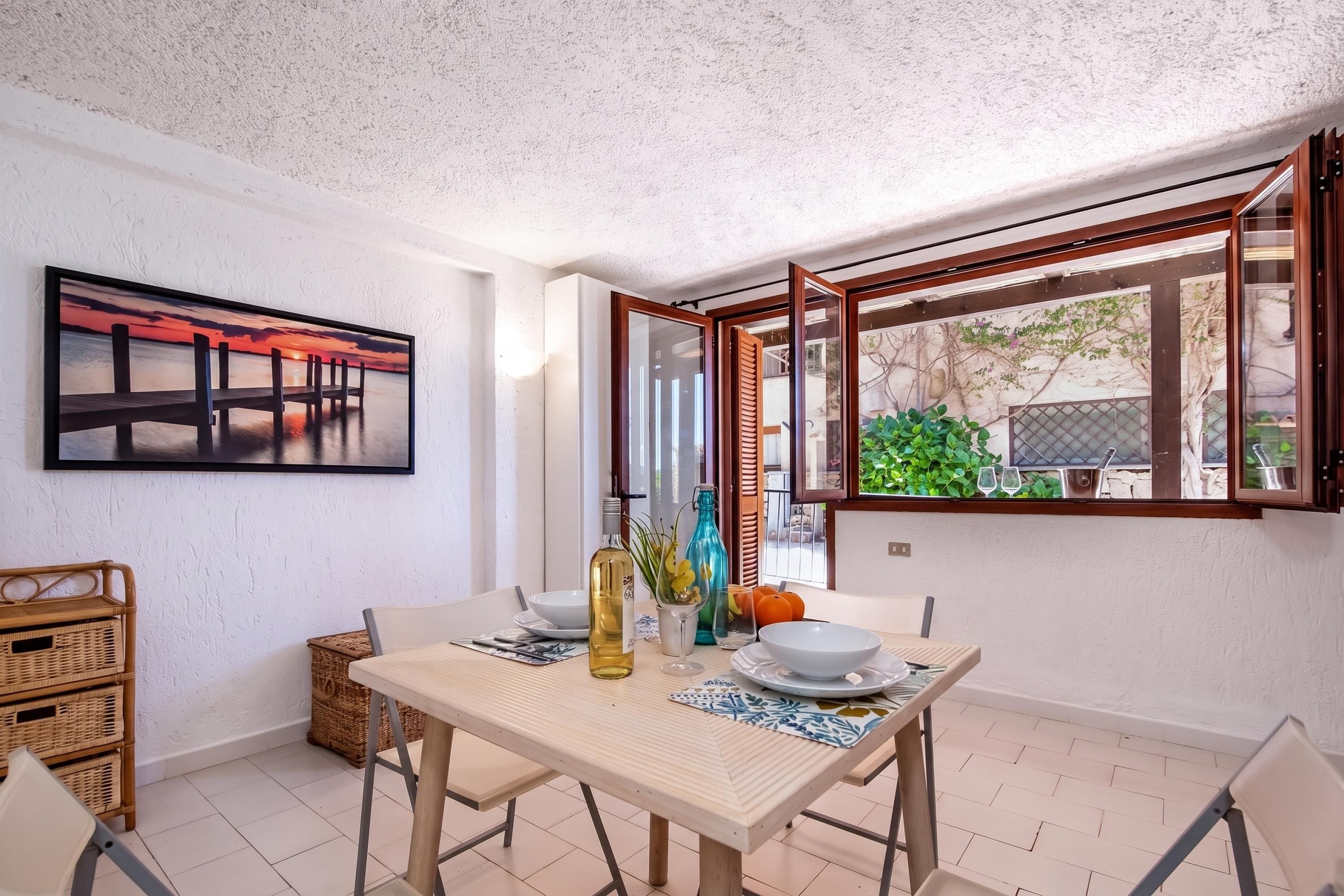 Ein Essbereich mit Tisch für zwei Personen, einem Gemälde an der Wand und Blick durch ein offenes Fenster.