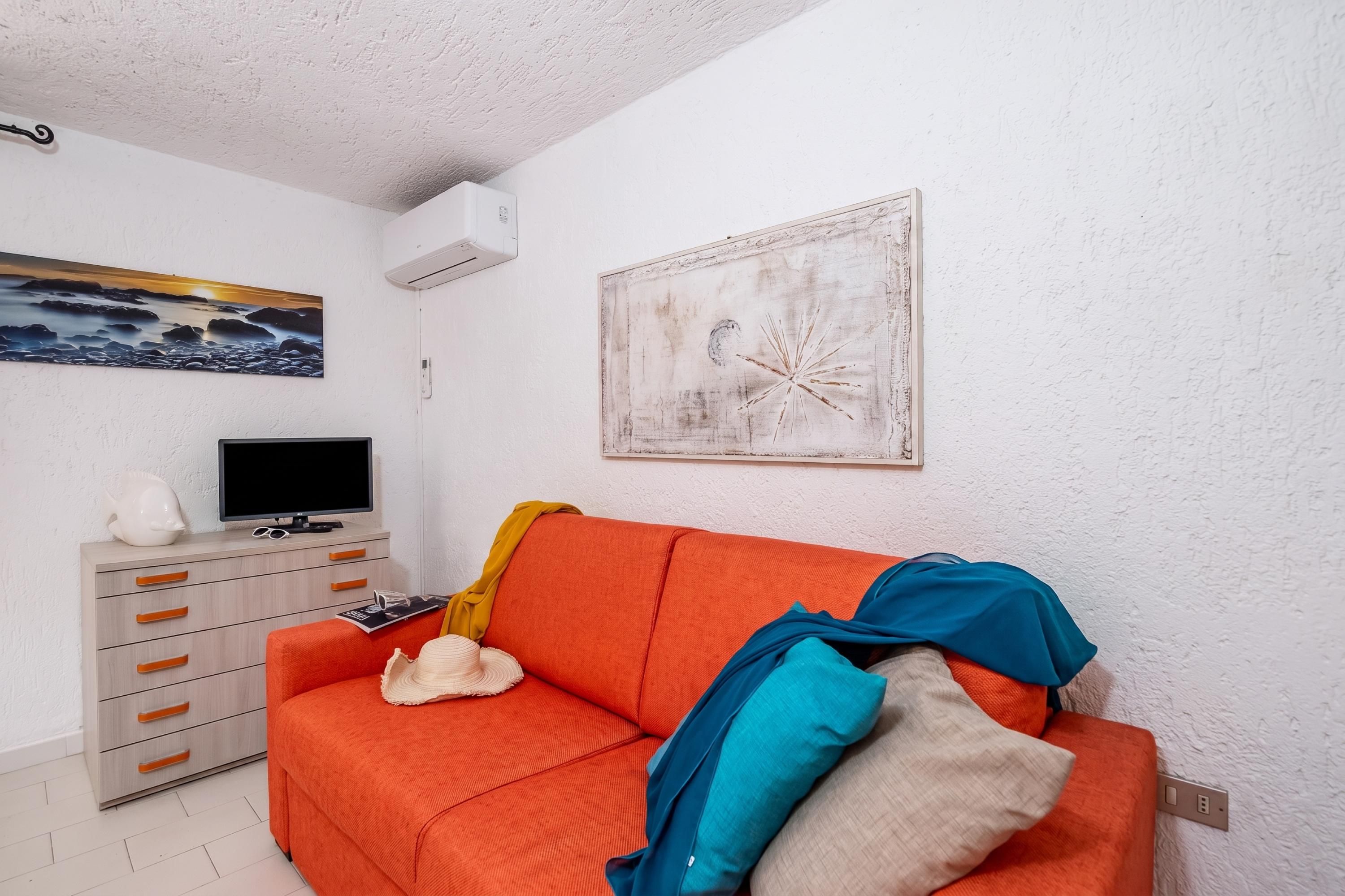 A living room with a sofa, a television, a painting, and a white wall.