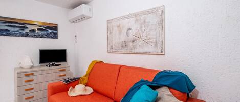 A living room with a sofa, a television, a painting, and a white wall.