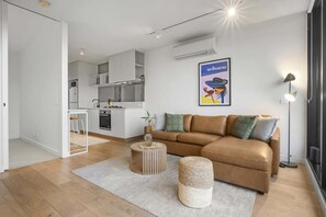 A modern apartment with a kitchen, a living area with a sofa and ottoman, and a framed artwork on the wall. - Bright 1-Bed Stay Near Crown Melbourne (South Melbourne)