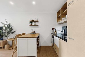 A compact kitchen with white cabinetry, a wooden dining table, and a small island. - Bright 1-Bed Apartment in Neutral Bay (Neutral Bay)