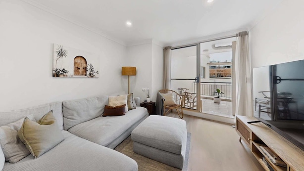 En moderne stue med sofa, fjernsyn og balkon med udendørs møbler.