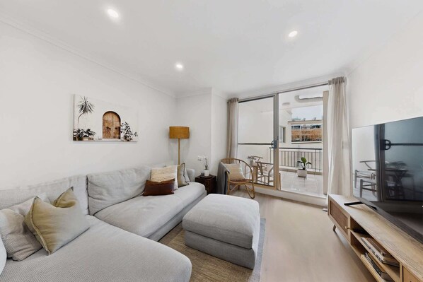 A modern living room with a sofa, a TV, and a balcony with outdoor furniture. - Bright 1-Bed Apartment in Neutral Bay (Neutral Bay)