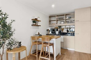 A compact kitchen with wooden cabinets, a dining area with two chairs, and a small table. - Bright 1-Bed Apartment in Neutral Bay (Neutral Bay)