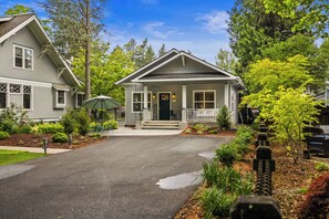 A residential house with a front porch, a driveway, and a garden with various plants and a small tree.