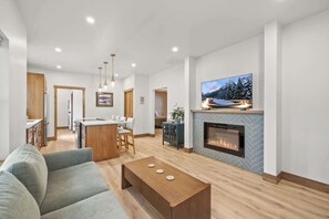 A modern living room with a fireplace, a television mounted above it, and a dining area in the background.