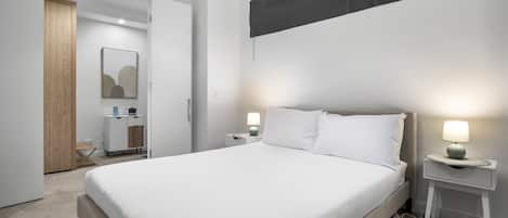 A modern hotel room with a large bed, bedside lamps, a small bedside table, and a wardrobe.