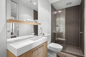 A modern bathroom with a double sink, a toilet, and a shower area. - Poolside 2-Bed Apartment in South Yarra (South Yarra)