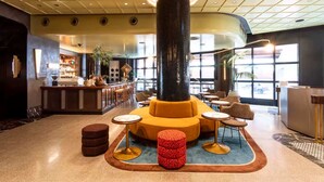 Eine Lobby mit einer zentralen Sitzecke, einer Bar und großen Fenstern.