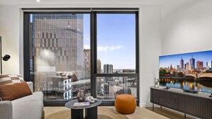 Ein modernes Wohnzimmer mit großem Fenster, Flachbildfernseher und einer Couch.