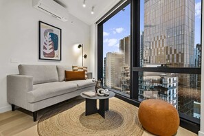 A modern living room with a grey sofa, a round coffee table, and a large window offering a city view. - High-Rise 2-Bed Stay at Queensbridge (Southbank)
