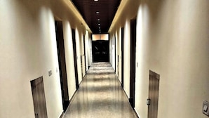 A long, narrow hallway with a polished floor, doors on both sides, and recessed lighting on the ceiling. - Hotel Vrindavan Paradise & Resort (Mathura)