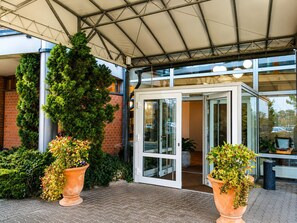 Une entrée d’immeuble avec une porte vitrée, une allée couverte et des plantes en pot.