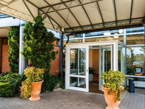 Une entrée abritée avec une porte vitrée, des plantes en pot et un mur de briques.