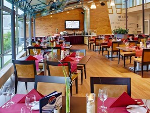 Un restaurant avec de nombreuses tables dressées pour le service, une scène pour les présentations et un mur de briques orné d’enseignes.