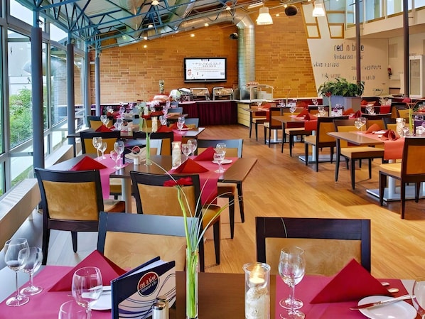 A restaurant with multiple tables set for dining, a stage for presentations, and a brick wall with signage. - 1 Person Holiday Park Home in Brauschweig (Braunschweig)