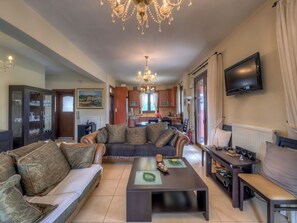 A living room with a sofa, coffee table, TV, and a dining area with a kitchen in the background. - Hidden Gem in Crete — Totally Private Villa for up to 9 Guests (Rethymno)
