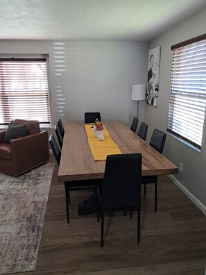 A modern living room with a wooden dining table, black chairs, a brown leather sofa, and a yellow rug. - Victory House. Close to Lambeau Field! (Green Bay)