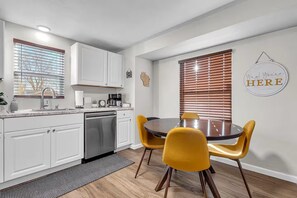 Una cocina moderna con armarios blancos, un lavavajillas de acero inoxidable y una mesa redonda con sillas amarillas.